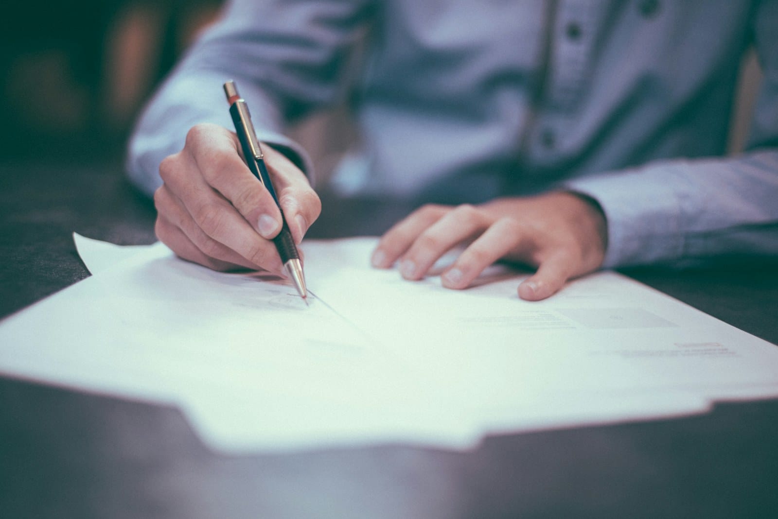 A hand signing a document, representing evidence-led correction of the record at the source.